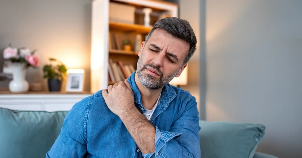 Relieving Chronic Shoulder Pain: How ESWT Helps Rotator Cuff and Tendon Conditions Heal Man holding a painful shoulder while sitting on a sofa